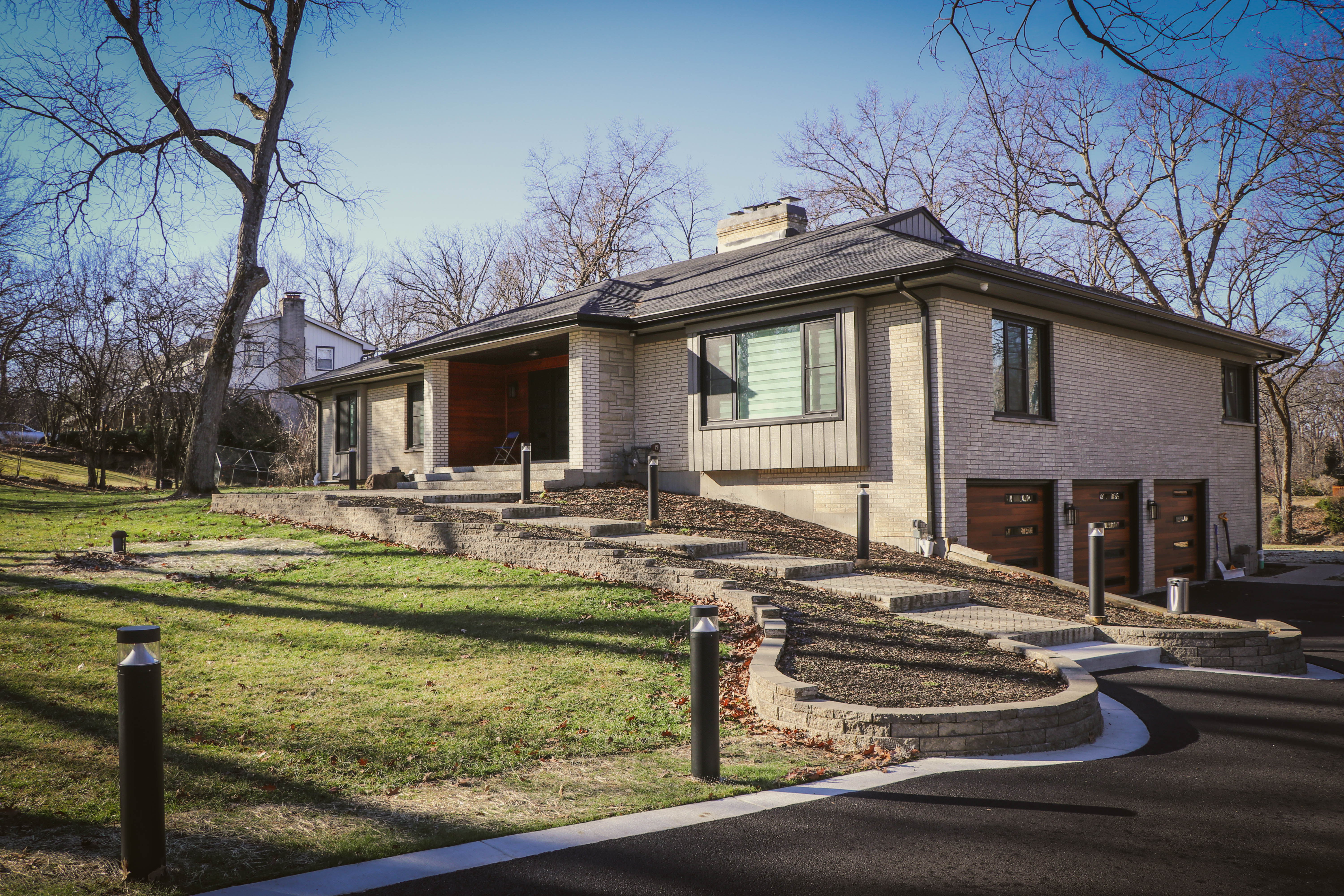 Front-of-house view showing the same paver driveway entrance with tiered stone retaining wall and walkway.