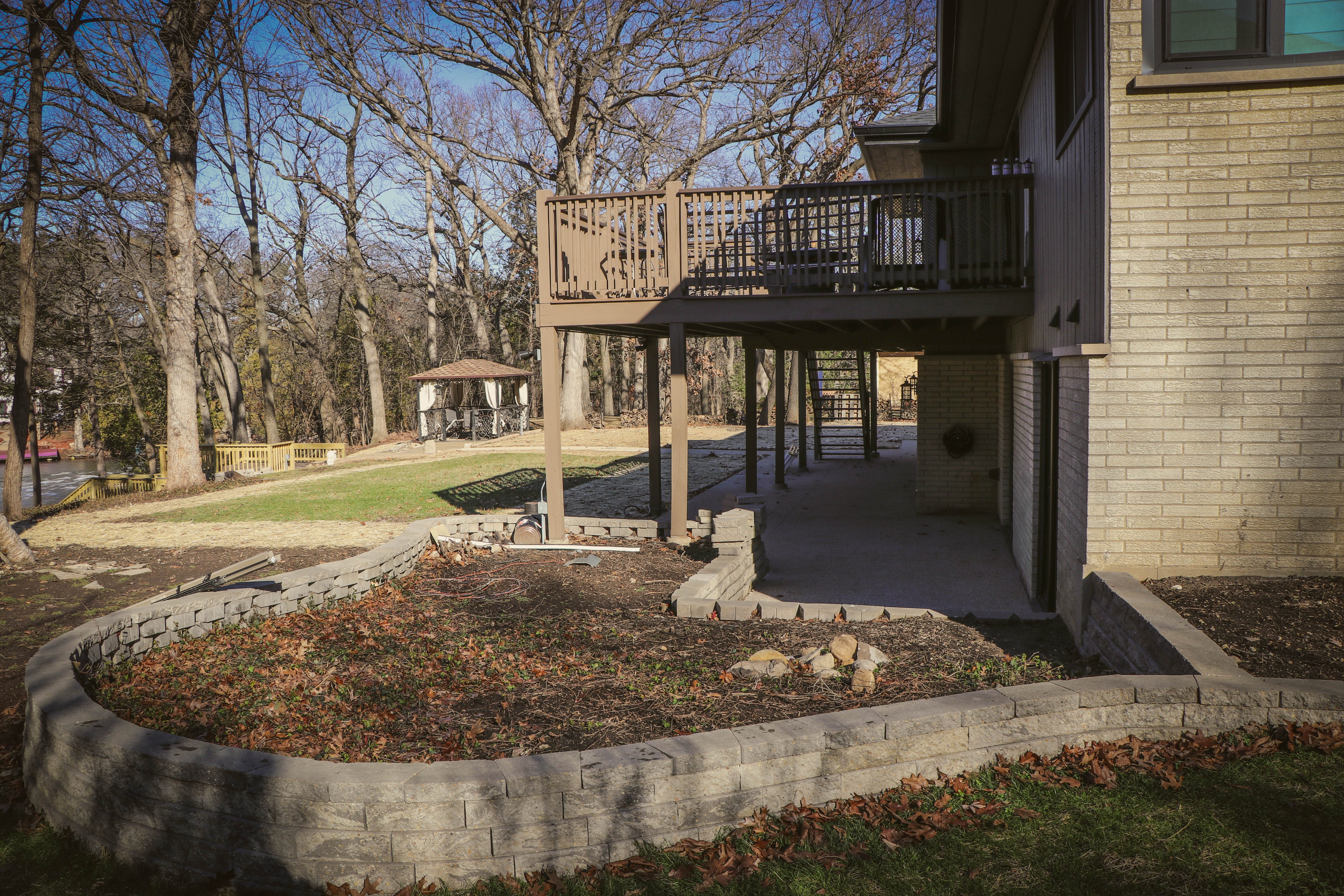 Wraparound deck and stone retaining bed wall above a paver patio at a Chicagoland residence — landscape design and install by Exotic Pavers and Landscaping.